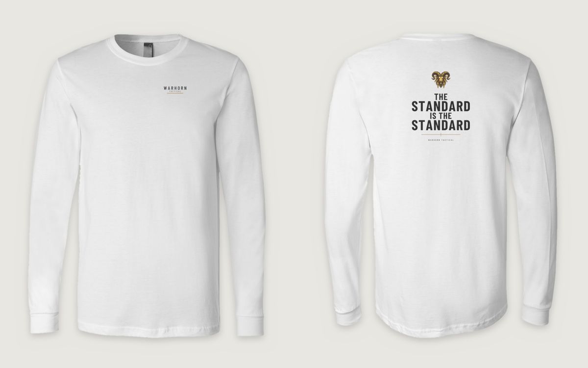 The Standard Long Sleeve in White shown front and back: WARHORN TACTICAL lockup with a gold underline, left chest; back: Full-color Warhorn ram over “The Standard Is the Standard,” a gold crosshair rule and a small WARHORN TACTICAL signature
